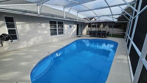 Une piscine avec un patio couvert, une clôture blanche et du mobilier d’extérieur.