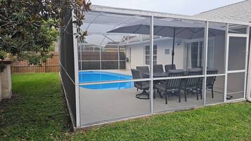 A screened outdoor area with a pool, patio furniture, and a view of a house in the background.