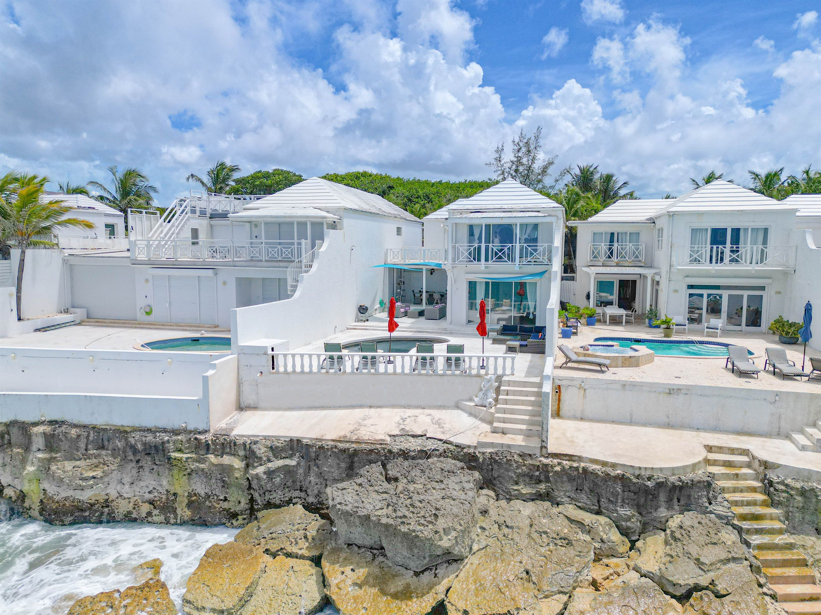 A beachfront property with multiple swimming pools, a staircase leading to a balcony, and a view of the ocean.