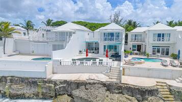 A beachfront property with multiple swimming pools, a staircase leading to a balcony, and a view of the ocean.