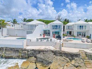 A beachfront property with multiple swimming pools, a staircase leading to a balcony, and a view of the ocean. - Caprice 5 - 3BR Oceanfront Villa with Pool (Nassau)