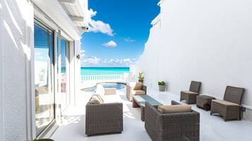 A sunlit outdoor patio with wicker furniture, a pool, and a view of the ocean.