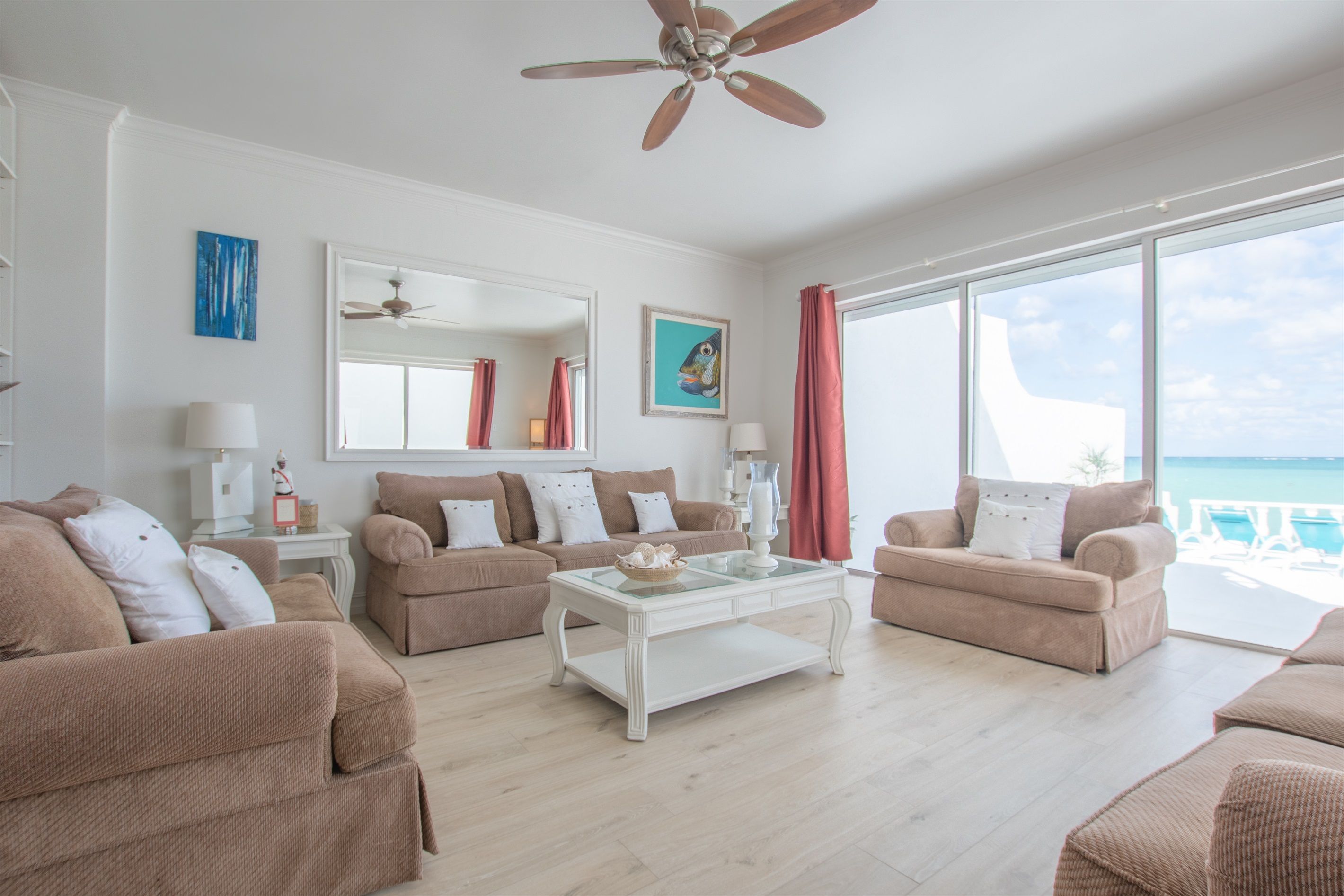 A spacious living room with a ceiling fan, large windows, and a view of the ocean.