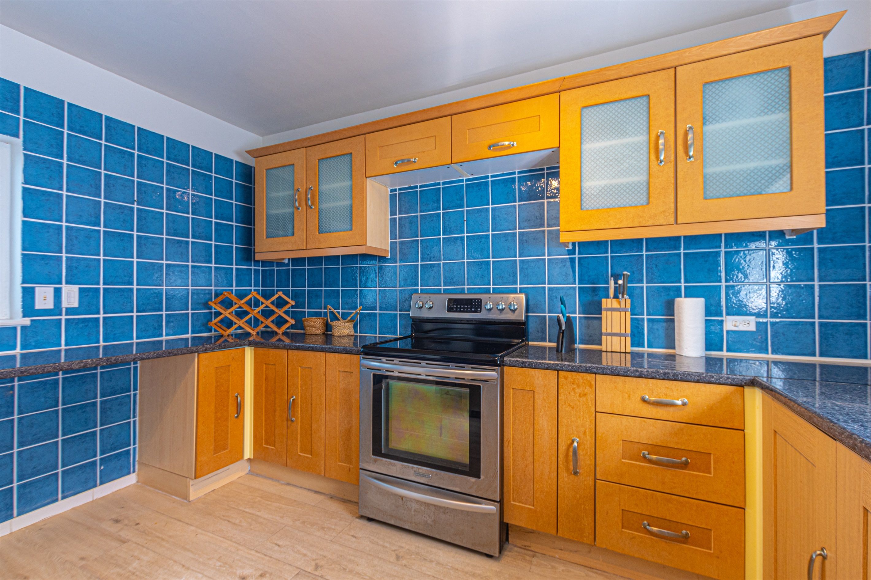 A kitchen with blue tiles, wooden cabinets, and stainless steel appliances.