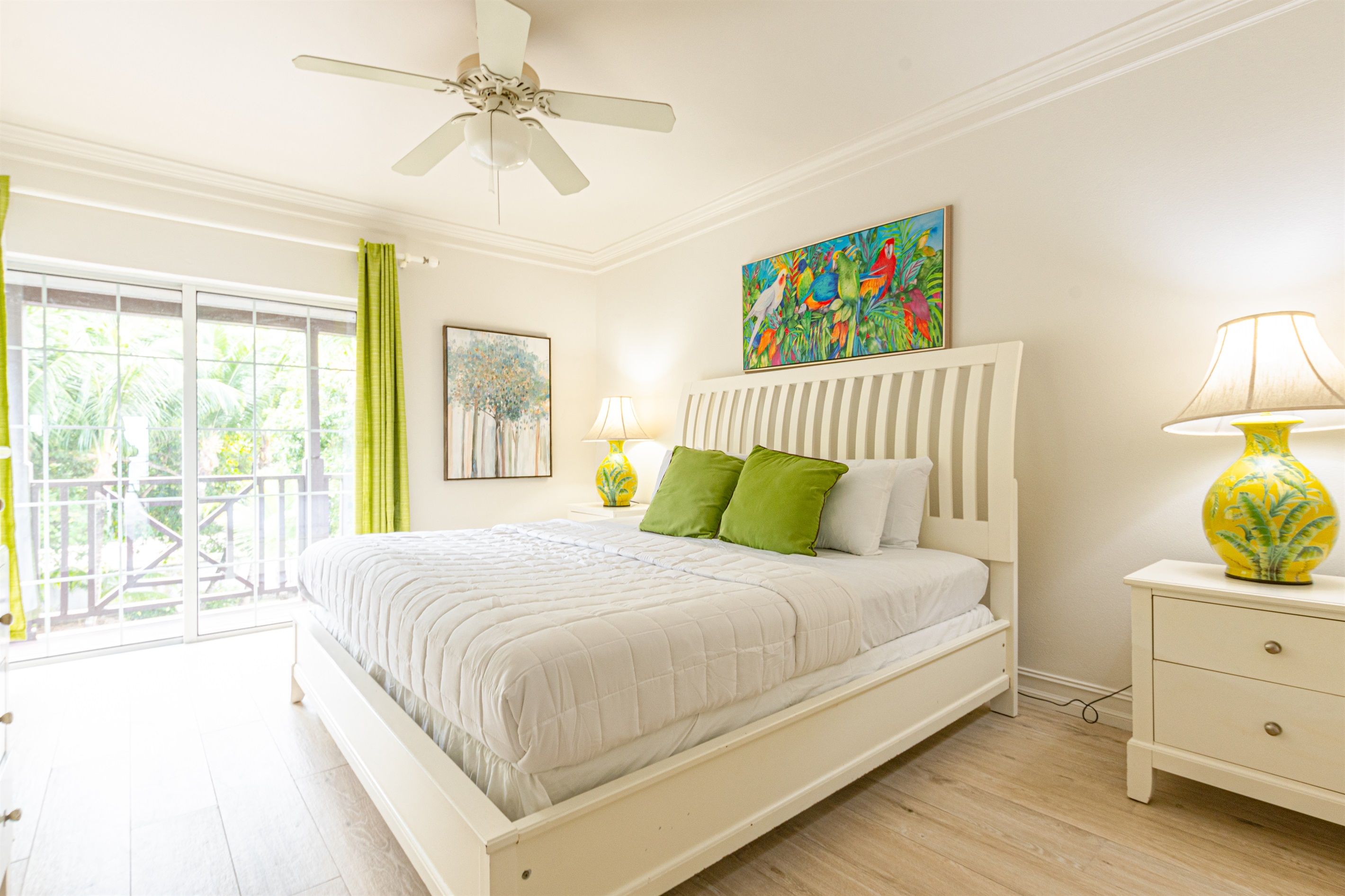 A bedroom with a bed, a nightstand, a ceiling fan, a window with curtains, and artwork on the wall.