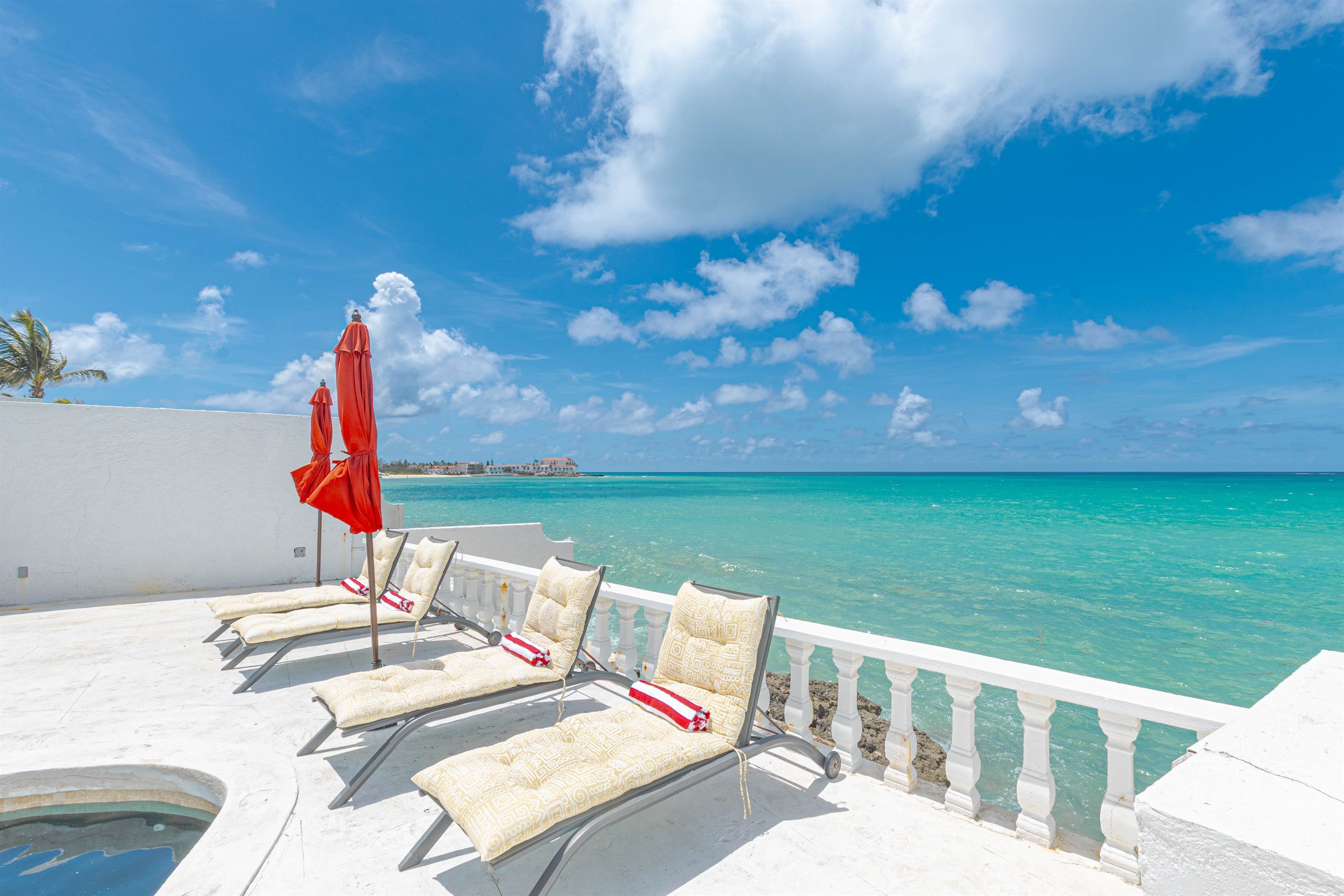 A poolside area with lounge chairs and a red umbrella, overlooking a clear blue sea.