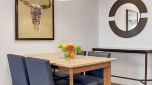 Un comedor con una mesa, sillas, un frutero, una obra de arte enmarcada y un espejo circular en la pared.