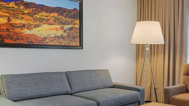 Una habitación con un sofá gris, una mesa de centro de madera, una lámpara de pie y un cuadro de un paisaje montañoso.