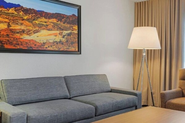 A room with a grey sofa, a wooden coffee table, a floor lamp, and a painting of a mountainous landscape.