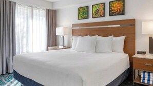 Habitación de hotel con una cama grande, cabecera de madera, mesita de noche con lámpara y tres cuadros en la pared.