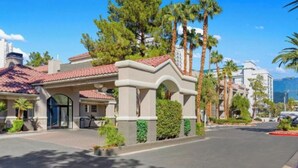 Un hotel con techo de tejas rojas, entrada con portón y palmeras.