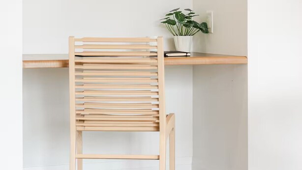 En trästol med ribbstöd i ryggen och benen, placerad framför en vit vägg och ett träbord.