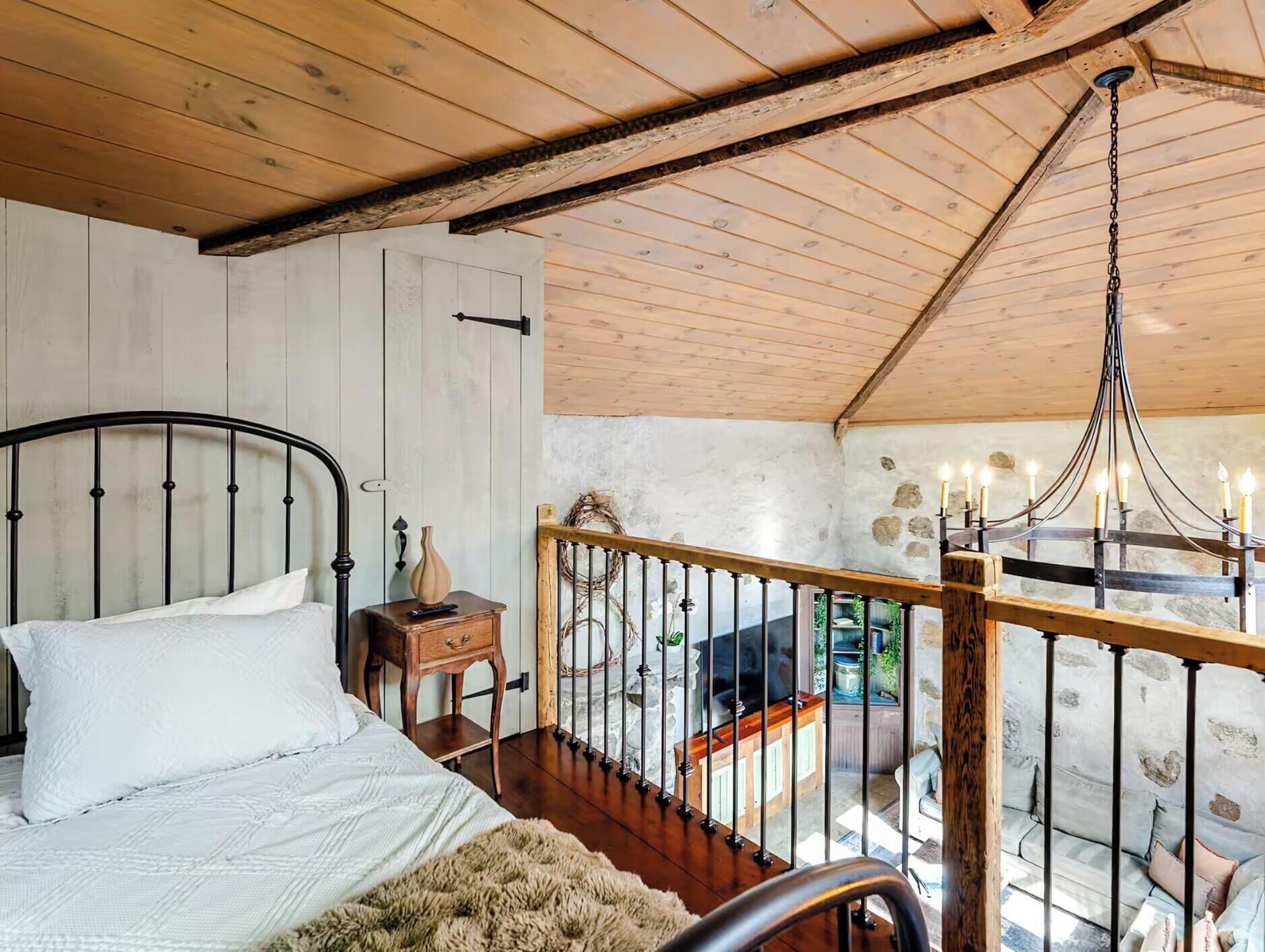 A bedroom with a bed, a nightstand, a wooden railing, and a chandelier.
