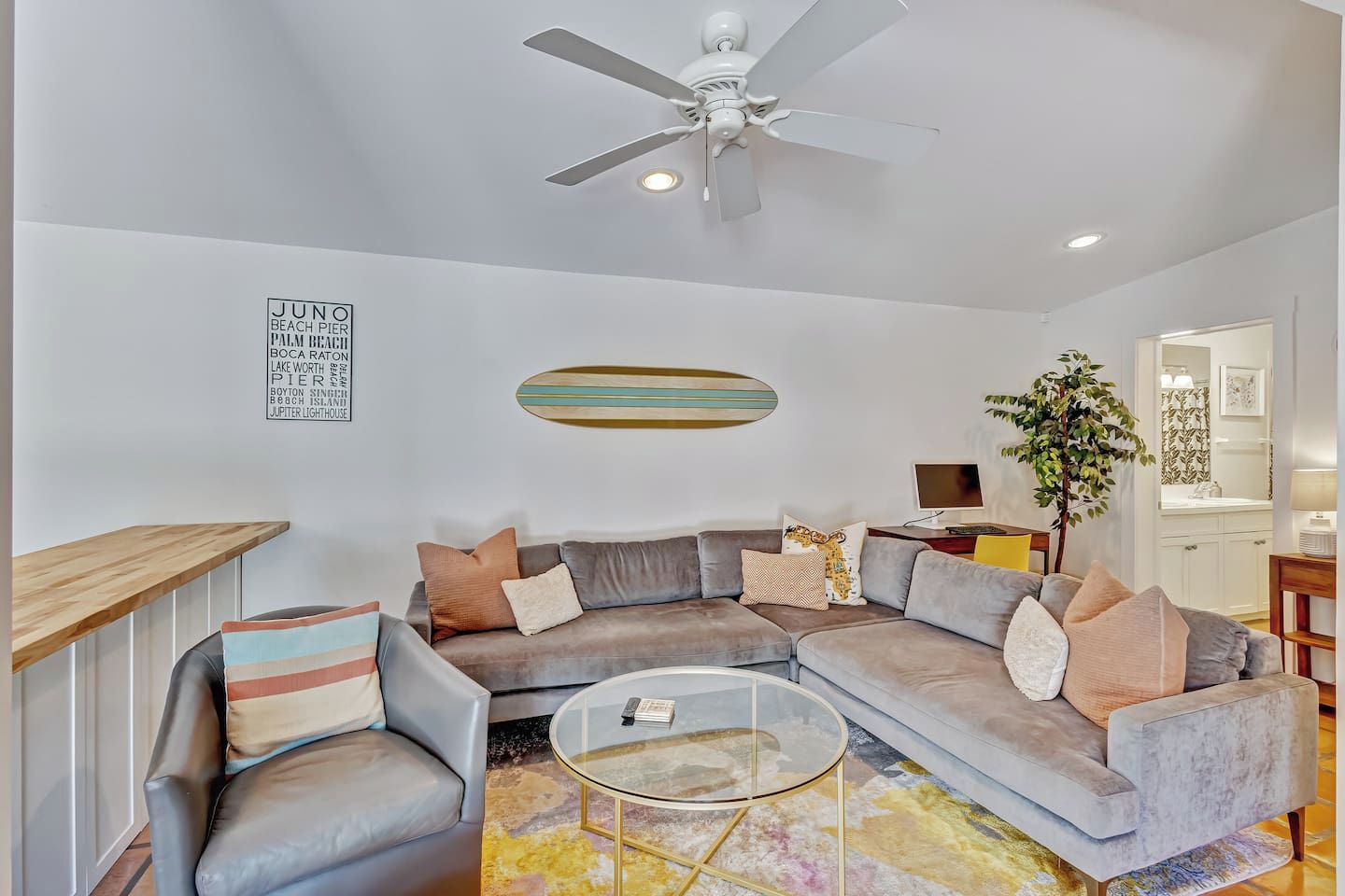 Un salon moderne avec un canapé d’angle, une table basse en verre et un ventilateur de plafond.