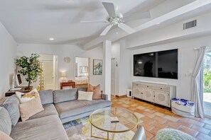A modern living room with a sofa, a glass coffee table, a television, and a ceiling fan. - The Key West House | Tropical Oasis |Close 2 Beach (West Palm Beach)