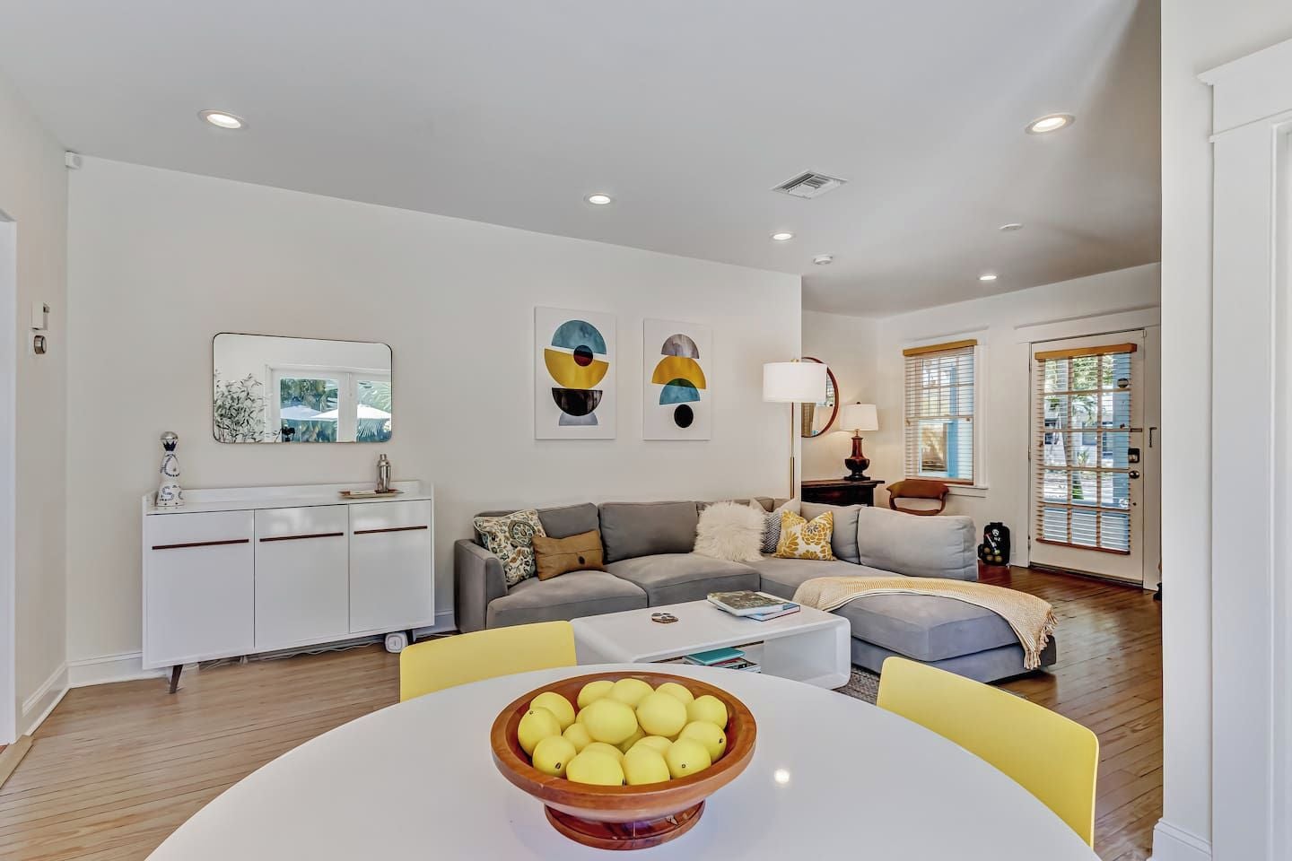 A modern living room with a sofa, a dining table with a bowl of fruit, and a white cabinet.