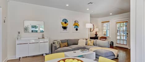 A modern living room with a sofa, a dining table with a bowl of fruit, and a white cabinet.