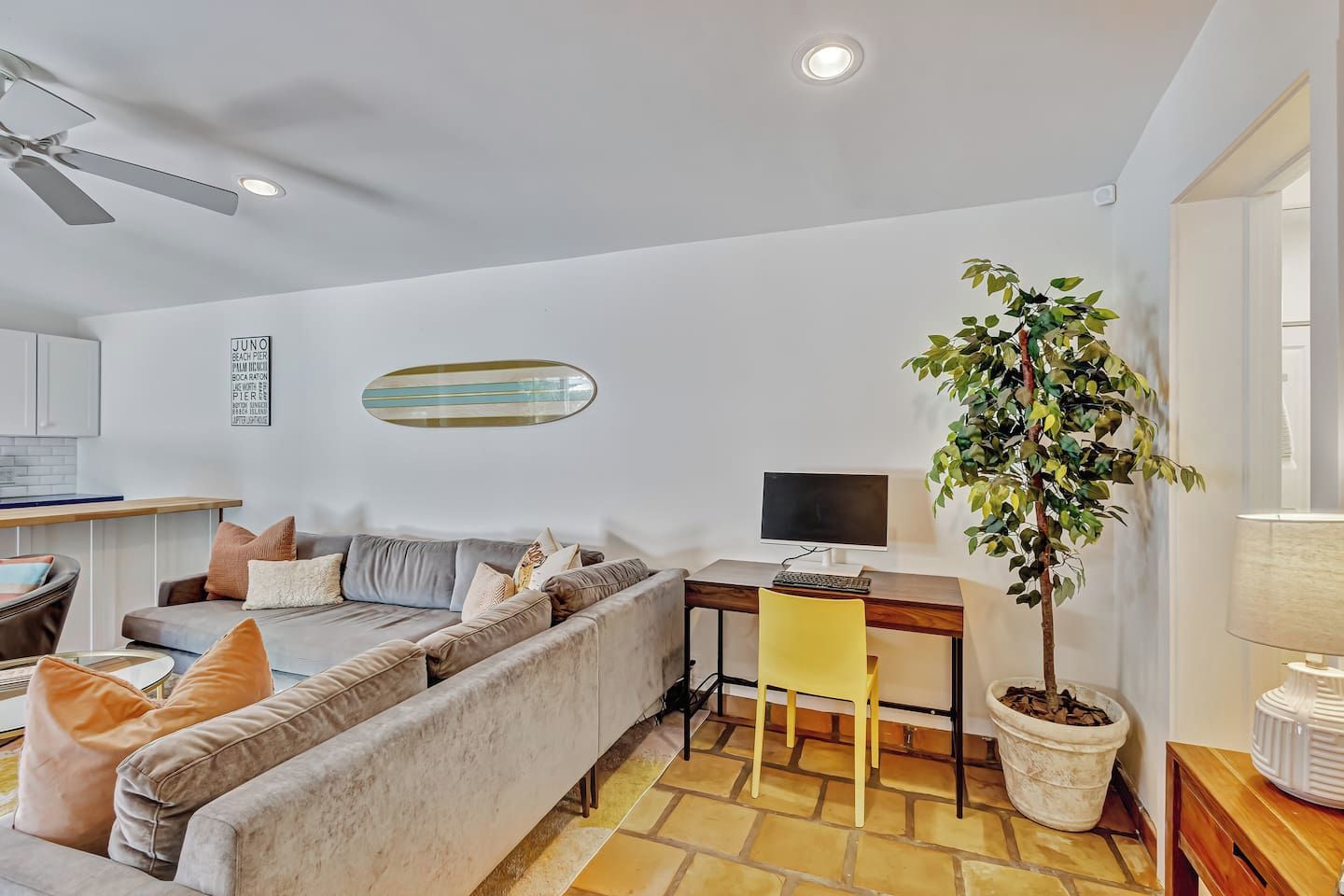 Un salon moderne avec un canapé, un bureau avec un ordinateur, un ventilateur de plafond et une plante en pot.