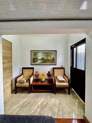 Una habitació amb dues cadires de fusta, una taula petita amb un ram de flors i un quadre a la paret.