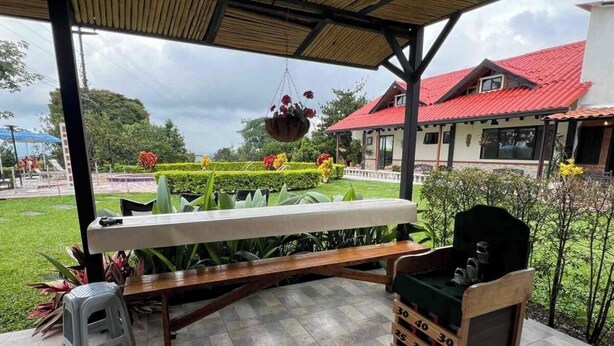 An outdoor covered patio with a wooden table, a grill, and a small stool. - Hacienda Familiar - Estancia 30P - Wifi (Ulloa)