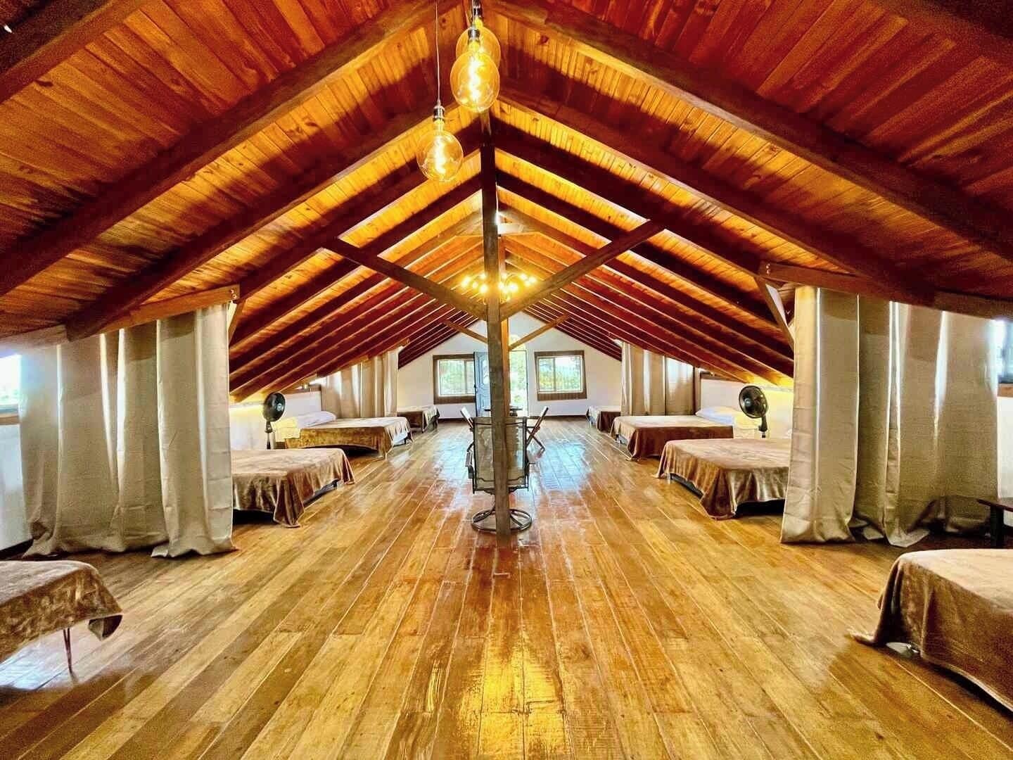 Ein geräumiges Dachzimmer mit Holzbalken, mehreren Betten und einer zentralen Leuchte.