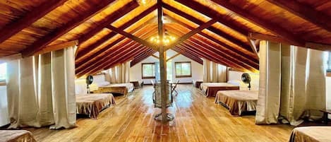 Amplia habitación en ático con vigas de madera, varias camas y un candelabro central.