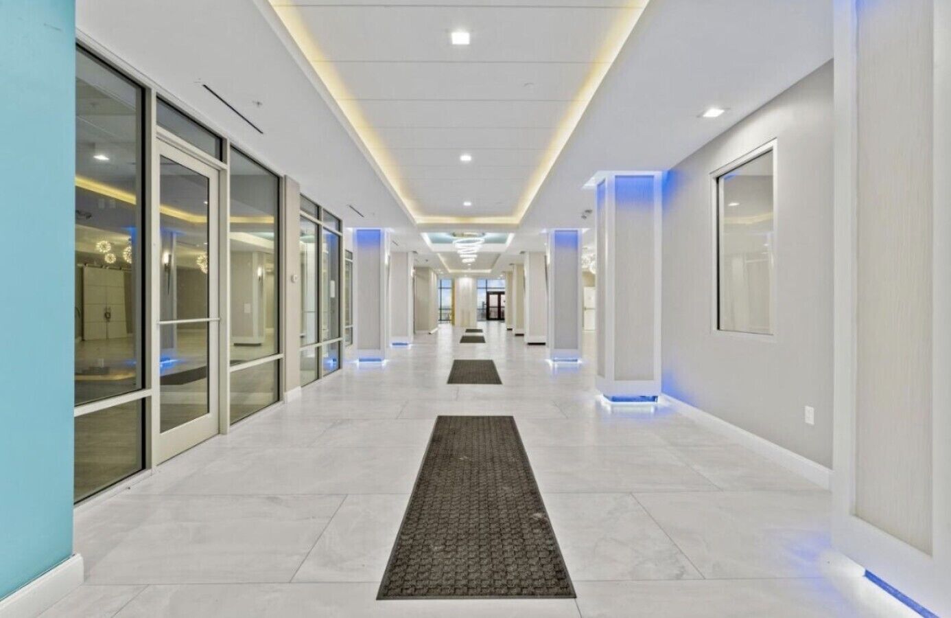 Um corredor moderno com portas de vidro, um tapete central e iluminação embutida.