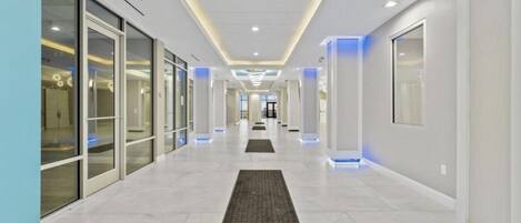 Un couloir moderne avec des portes en verre, un tapis central et un éclairage encastré.