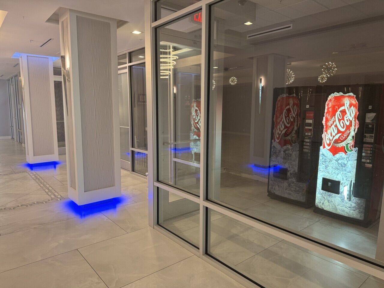 Um interior moderno com divisórias de vidro, uma máquina de refrigerantes Coca-Cola e pilares iluminados.