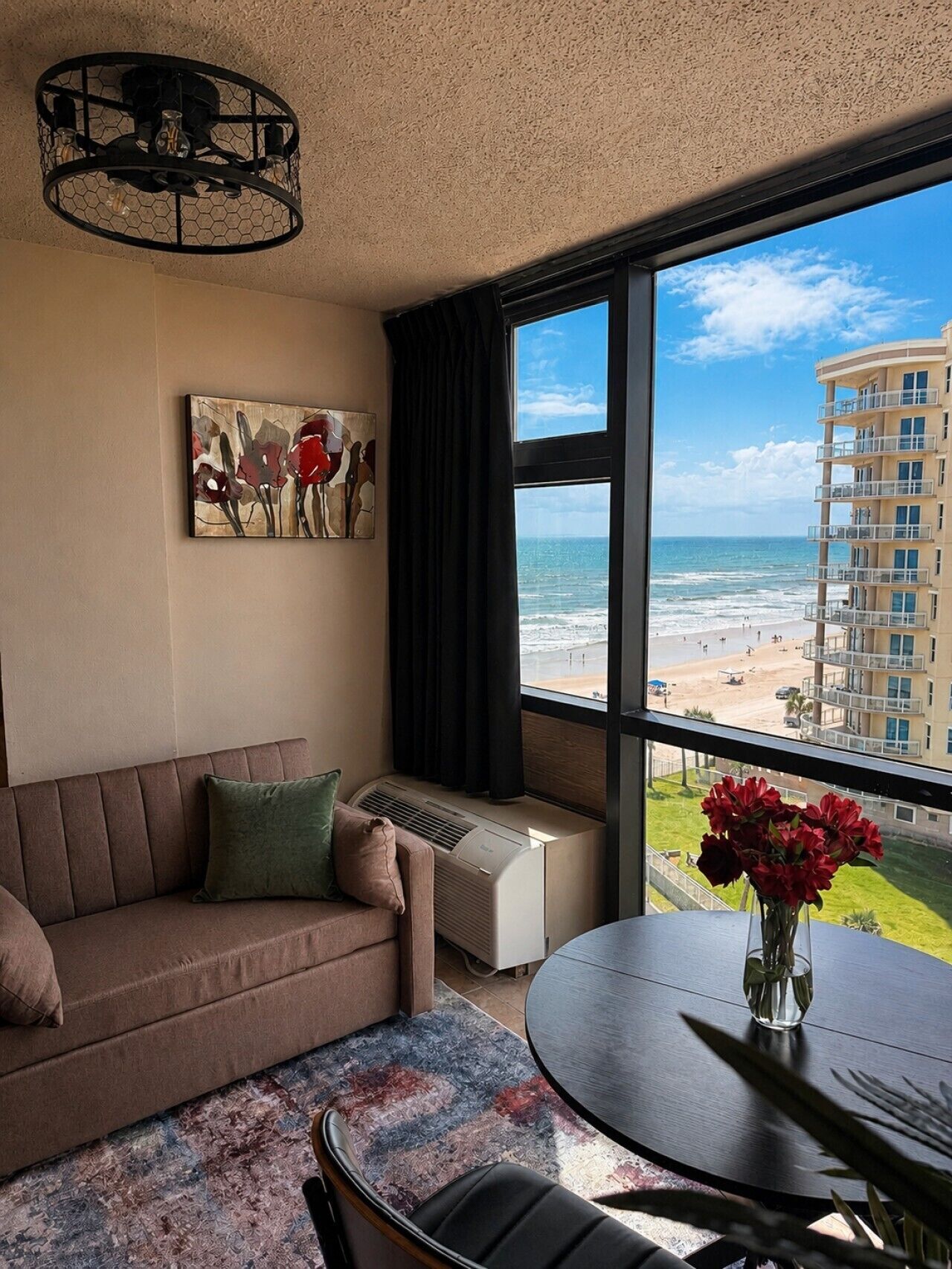 Quarto com vista para a praia, um sofá, uma mesa e um quadro na parede.