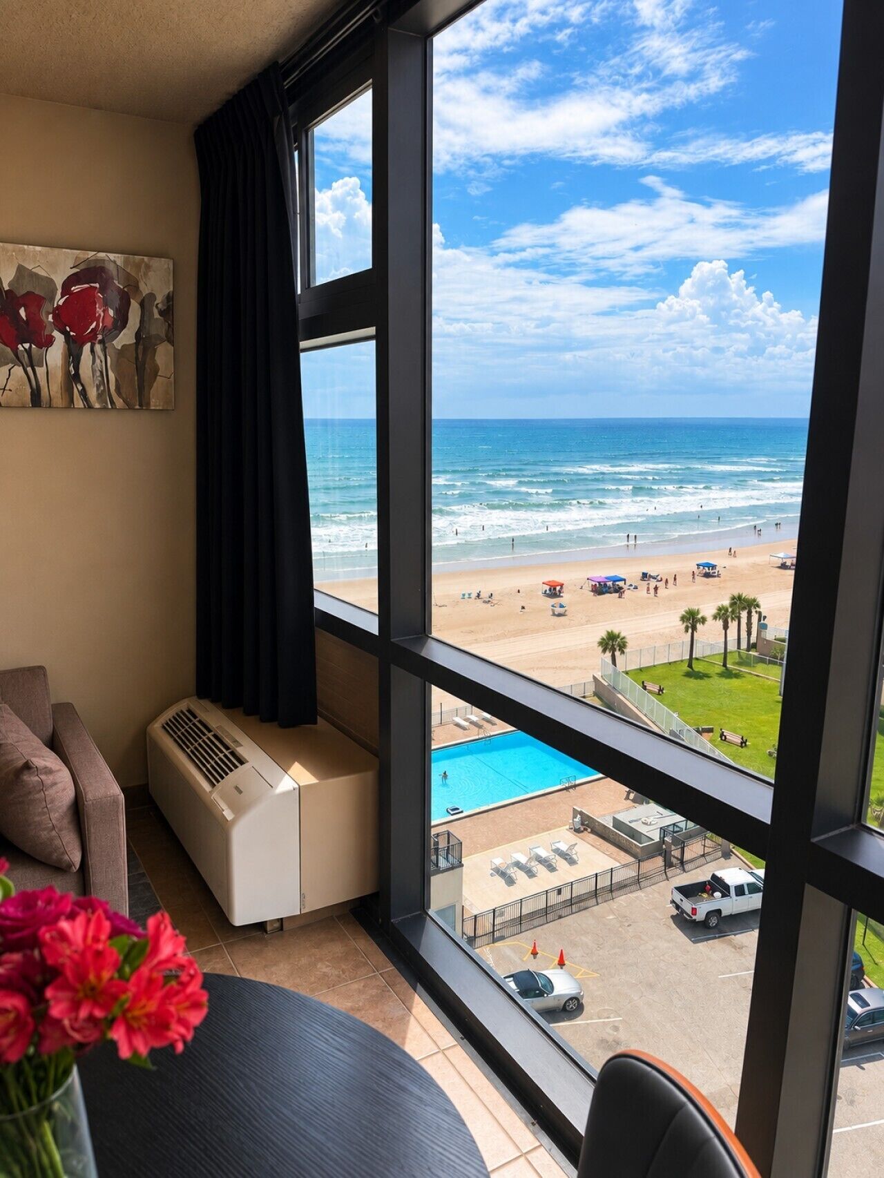 Une chambre dotée d’une grande fenêtre donnant sur une plage, une piscine et un parking.