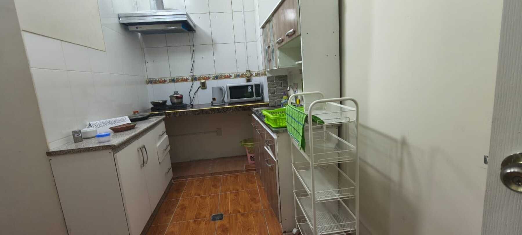 A compact kitchen with white cabinets, a microwave, a sink, and a green dish rack.