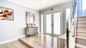 A modern interior with a wooden staircase, a large mirror, and a colorful abstract painting on the wall. - Private Oasis - Pool & Backyard (Hialeah)