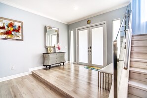 Ein modernes Interieur mit einer Holztreppe, einem großen Spiegel und einem farbenfrohen, abstrakten Gemälde an der Wand.