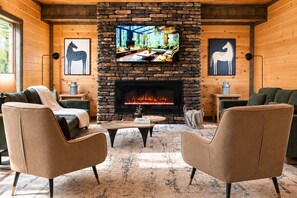 A cozy living room with a stone fireplace, comfortable seating, and a television mounted on the wall. - Luxury Smoky Retreat | Pool, Theater & Hot Tub (Sevierville)
