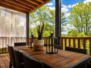 Eine Holzterrasse mit Tisch, Stühlen, einem Blumentopf und zwei Laternen.