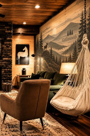 A cozy room with a hanging chair, a sofa, a lamp, and a wall mural depicting a mountain scene. - Luxury Smoky Retreat | Pool, Theater & Hot Tub (Sevierville)