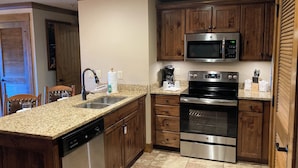 A kitchen with granite countertops, wooden cabinets, stainless steel appliances, and a dishwasher. - Cozy 1-bedroom condo with balcony in beautiful Gatlinburg with Water Park passes (Gatlinburg)