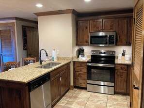 A kitchen with granite countertops, wooden cabinets, stainless steel appliances, and a dishwasher. - Cozy 1-bedroom condo with balcony in beautiful Gatlinburg with Water Park passes (Gatlinburg)