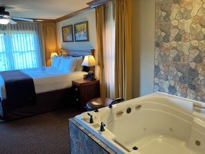 A hotel room with a large bed, a separate seating area with a chair, a bathtub, and a stone wall. - Cozy 1-bedroom condo with balcony in beautiful Gatlinburg with Water Park passes (Gatlinburg)