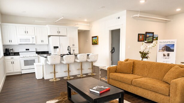 A modern living room with a sofa, a coffee table, and a kitchen area with white cabinets and appliances.