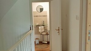 A hallway leading to a bathroom with a mirror, sink, and towel rack. - Vacation Home in a Rural Setting (Heidwiller)
