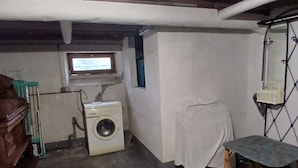 A laundry room with a washing machine, a wooden chair, and a small table. - Vacation Home in a Rural Setting (Heidwiller)