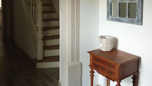 A hallway with a wooden staircase, a textured wall, and a small wooden table with a woven basket. - Vacation Home in a Rural Setting (Heidwiller)