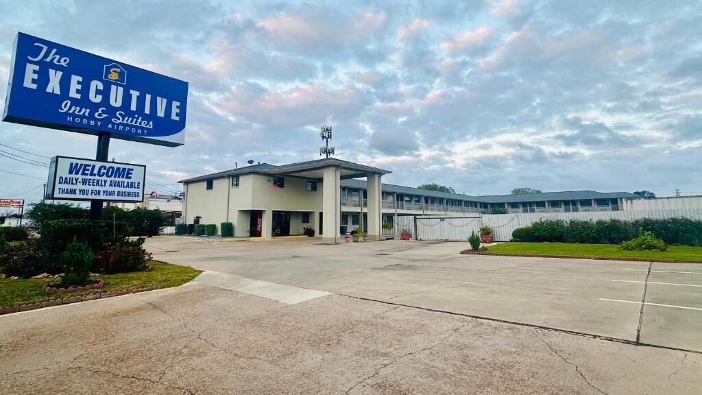A hotel named 'The Executive Inn & Suites' with a welcoming sign, a covered outdoor area, and a building with multiple windows.