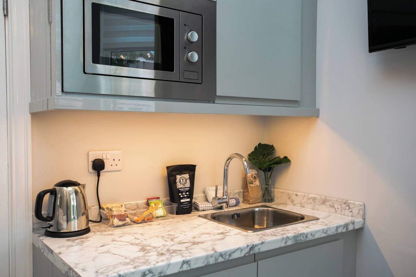 Una cocina equipada con microondas, hervidor de agua, pileta y encimera de mármol.