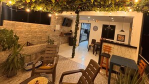 Un espacio al aire libre con mobiliario de madera, un muro de piedra y plantas colgantes.