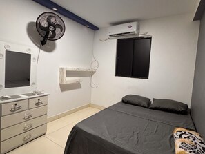 Un dormitorio con cama, cómoda, espejo, ventilador y aire acondicionado.