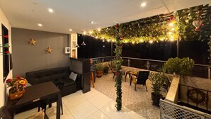 Una sala de estar moderna con un sofá, una mesita de centro y un televisor. Hay plantas y luces de cadena.