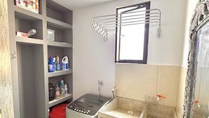 Una cocina funcional con lavadora, lavamanos y estantes con productos de limpieza.